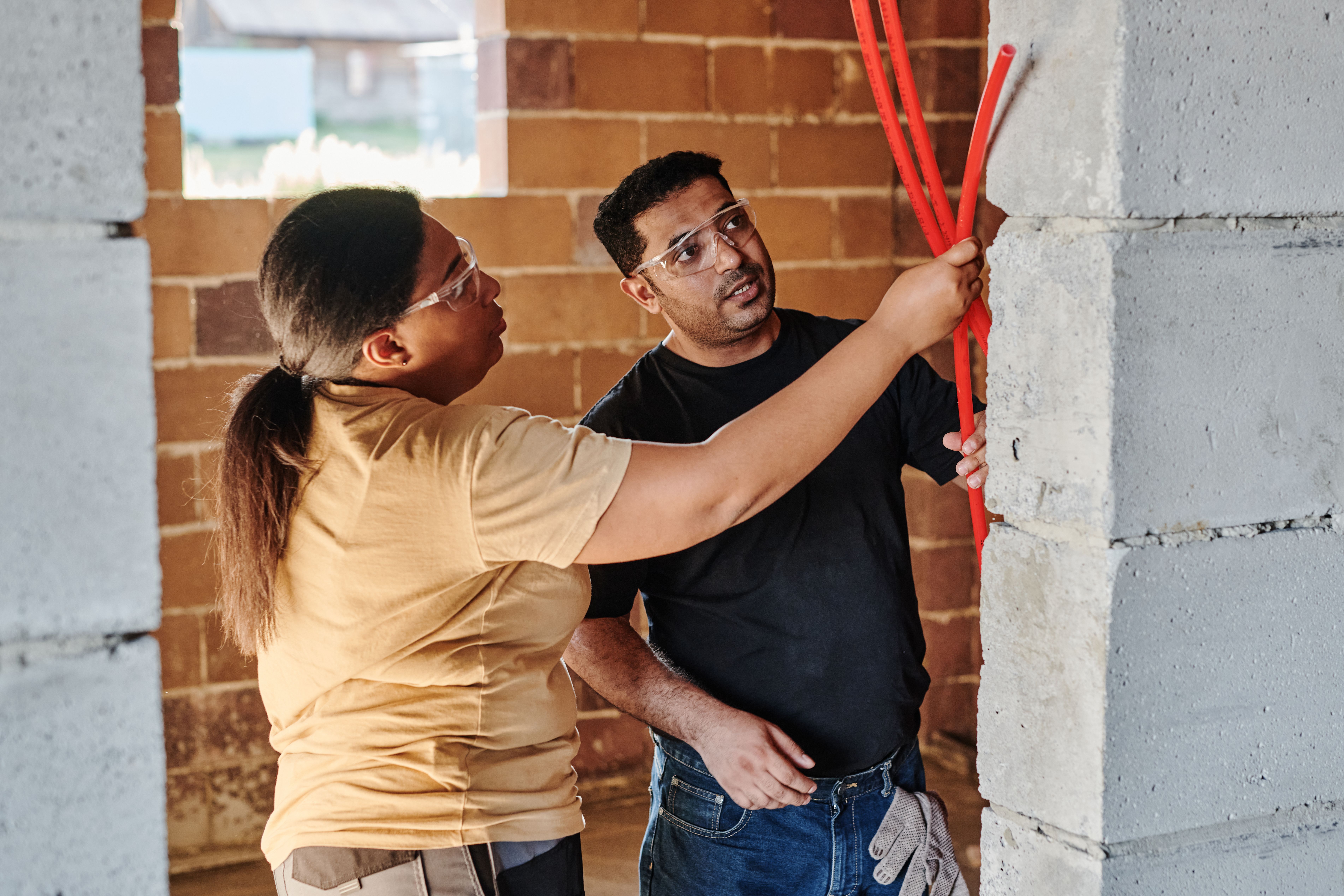 Electricians running conduit up a brick wall